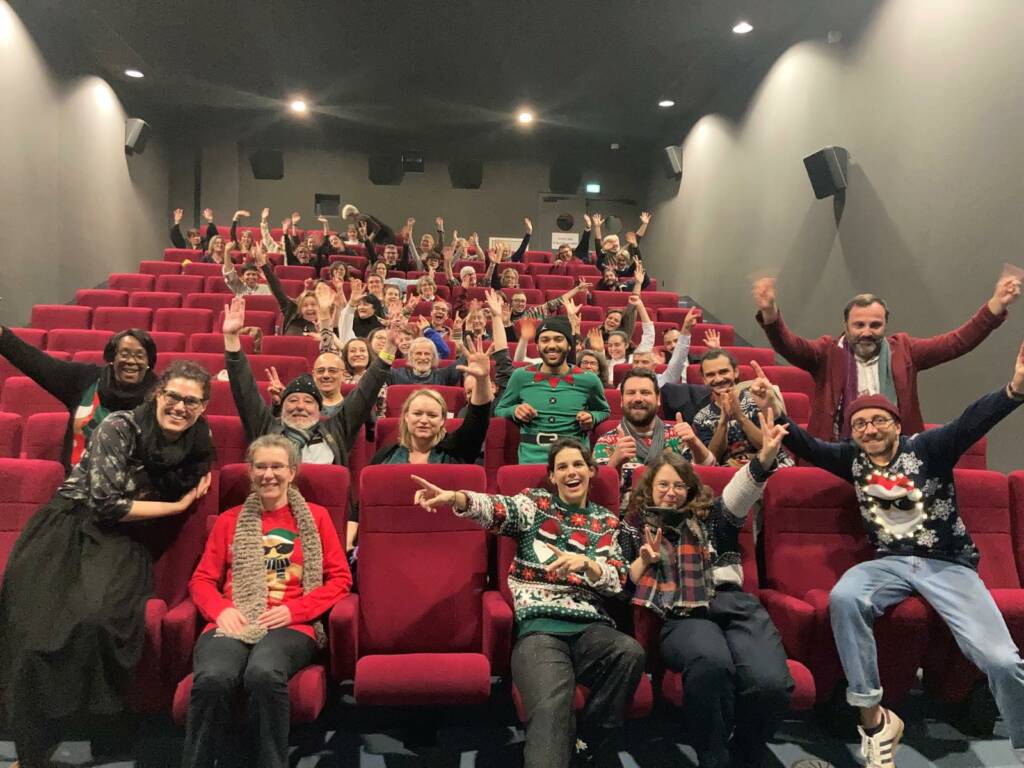 Du public dans une salle de cinéma lève les bras au ciel en souriant.