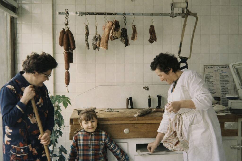 une vieille photo avec un petit garçon qui regarde vers nous et deux femmes beaucoup plus agées. Les trois personnes sont dans une cuisine des années 60-70.